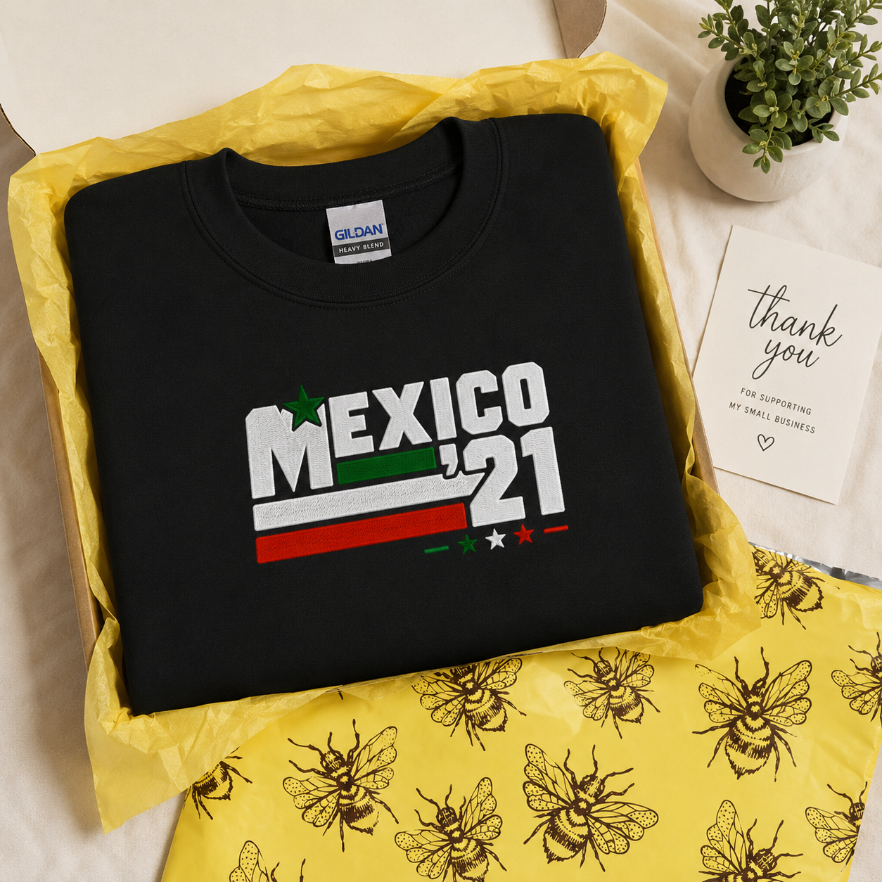 Black Gildan Heavy Blend crewneck sweatshirt featuring Embroiderzilla's retro Mexico '21 embroidered design packaged in a gift box with signature bee tissue paper and thank-you card.