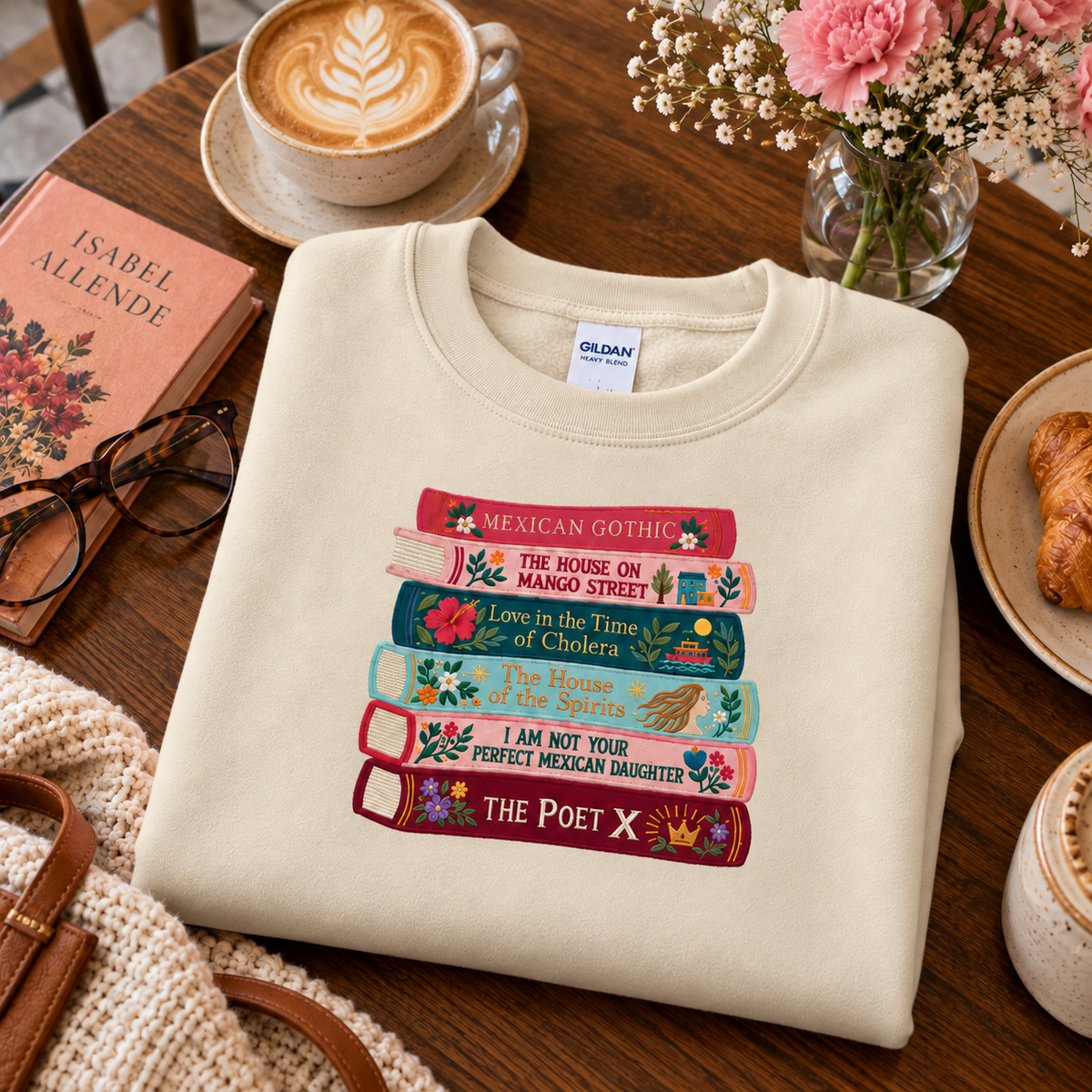 Sand-colored embroidered book stack sweatshirt styled with coffee, books, and flowers in a cozy flat lay.
